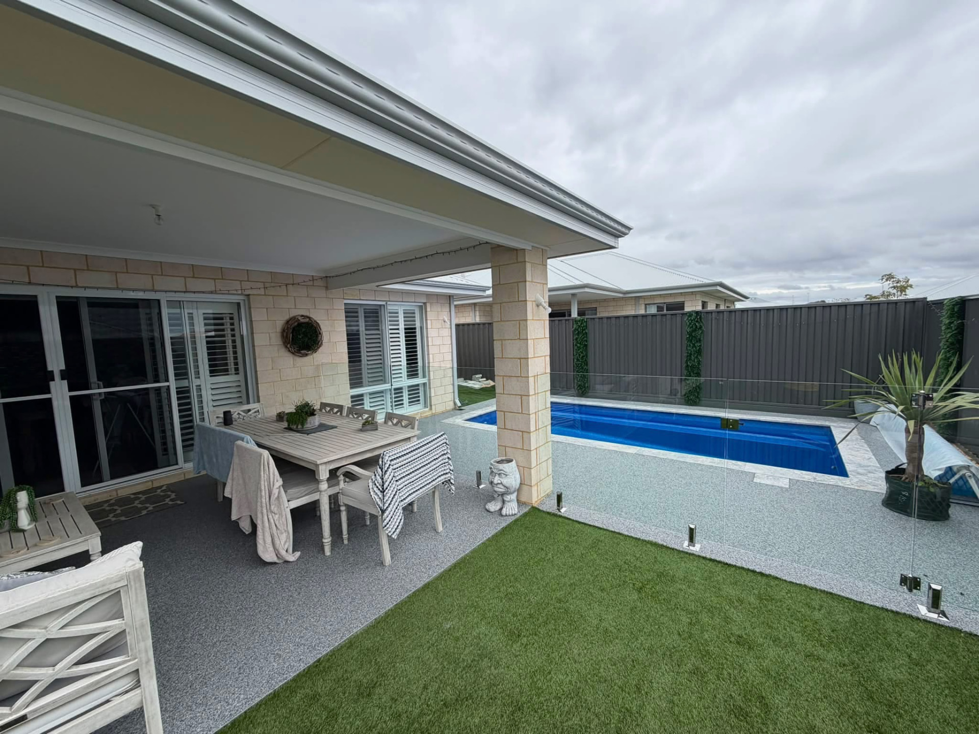 Resin bound alfresco dining patio adjoining a glass-fenced swimming pool