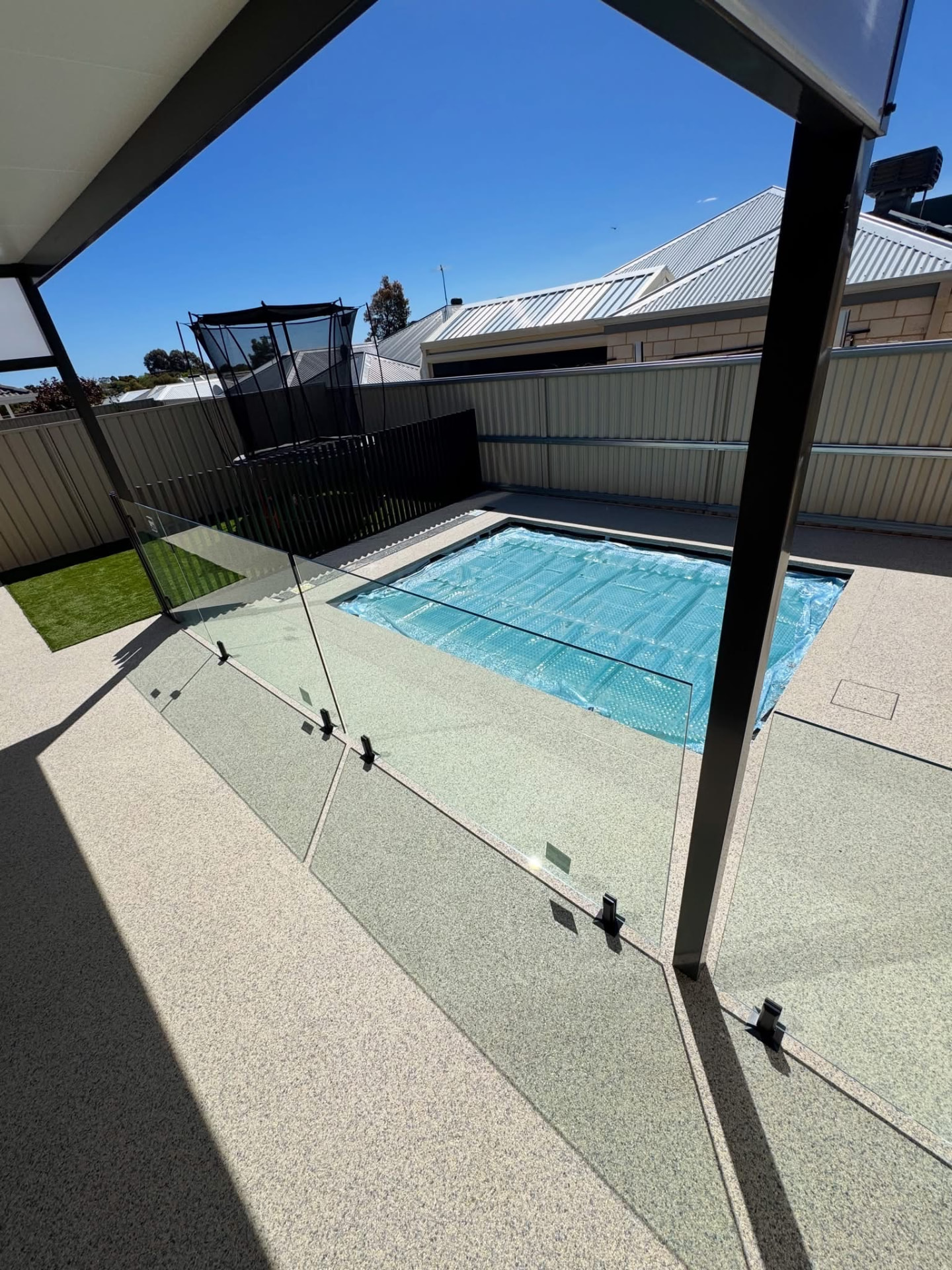 Light resin bound pool surround with glass fencing and covered patio