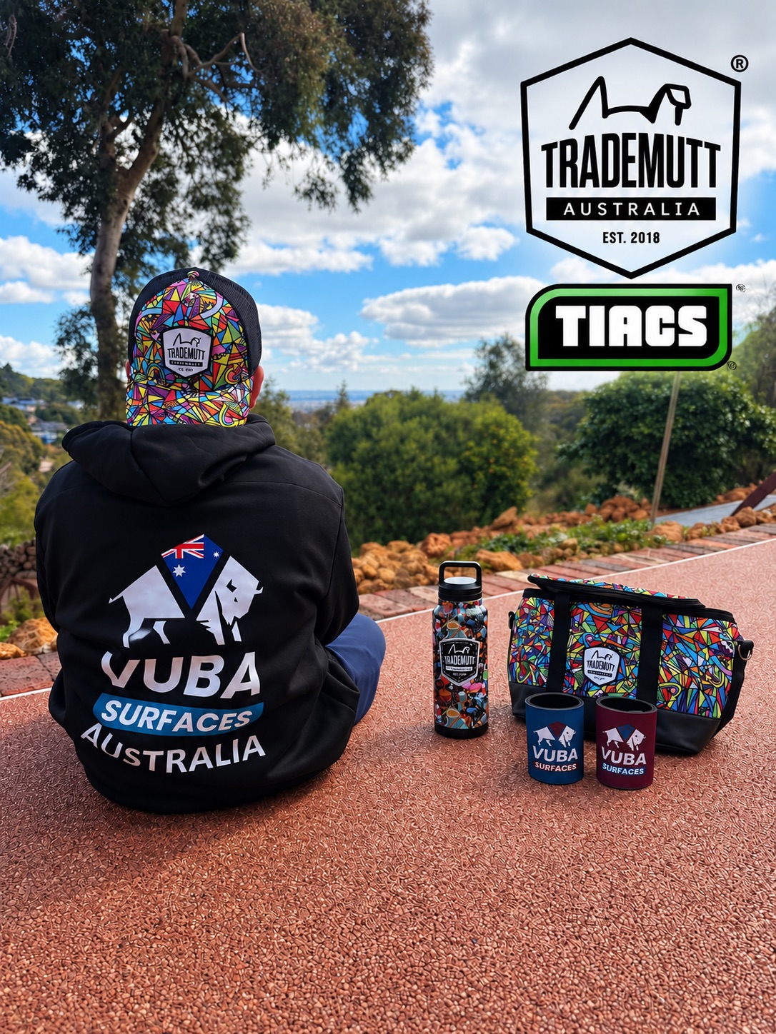 Person in a Vuba Surfaces hoodie and TradeMutt cap sitting beside TradeMutt gear looking out over bushland